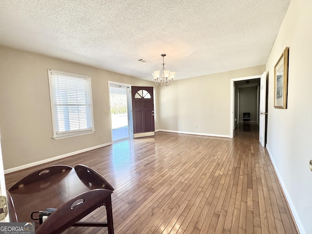 entryway featuring a chandelier, a textured ceiling, hardwood / wood-style flooring, visible vents, and baseboards