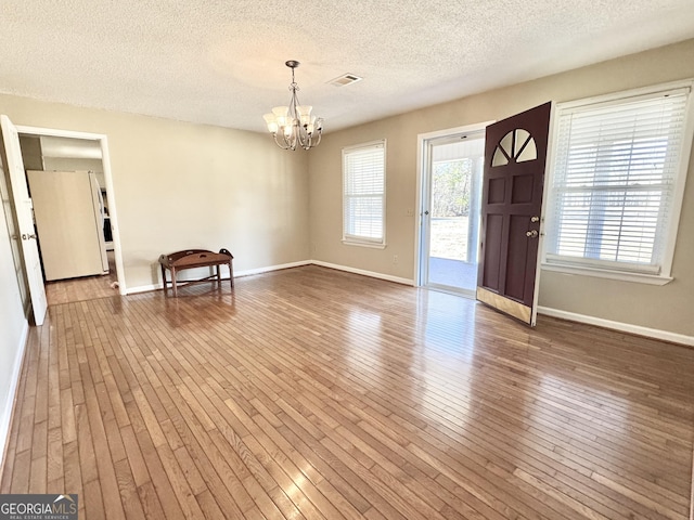 interior space with hardwood / wood-style flooring, baseboards, visible vents, and a chandelier