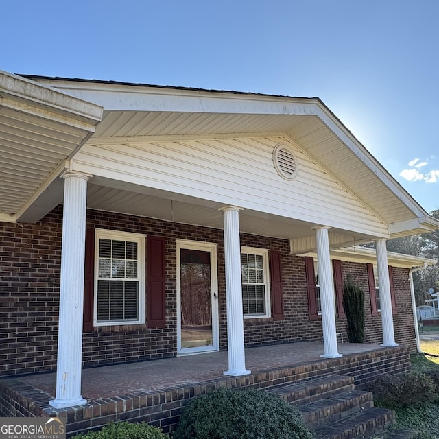 view of exterior entry with covered porch and brick siding