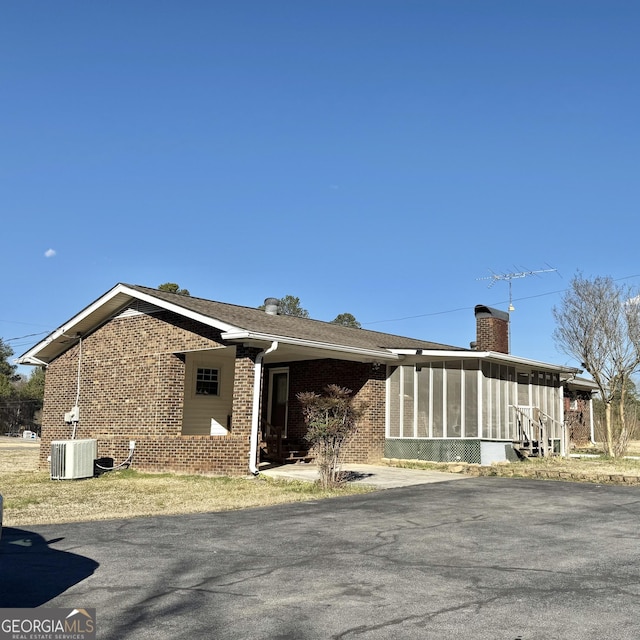 view of front facade featuring cooling unit, a sunroom, brick siding, and a chimney