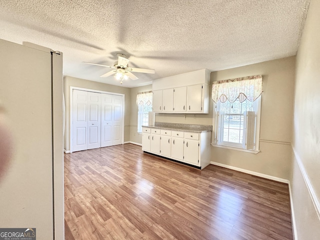 kitchen featuring light countertops, a ceiling fan, white cabinetry, light wood-type flooring, and baseboards