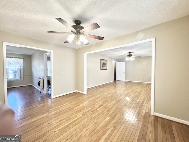 empty room with a textured ceiling, a ceiling fan, baseboards, heating unit, and light wood finished floors