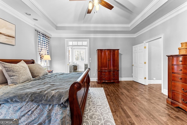 bedroom featuring a tray ceiling, dark wood-style flooring, ornamental molding, ceiling fan, and baseboards