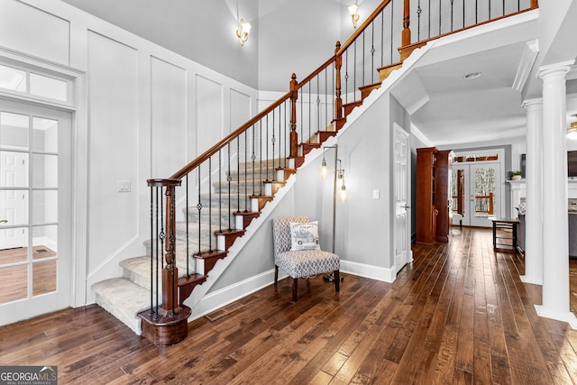 entrance foyer featuring a decorative wall, a high ceiling, stairway, wood-type flooring, and ornate columns