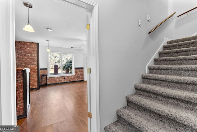 stairs featuring a brick fireplace, brick wall, and wood finished floors