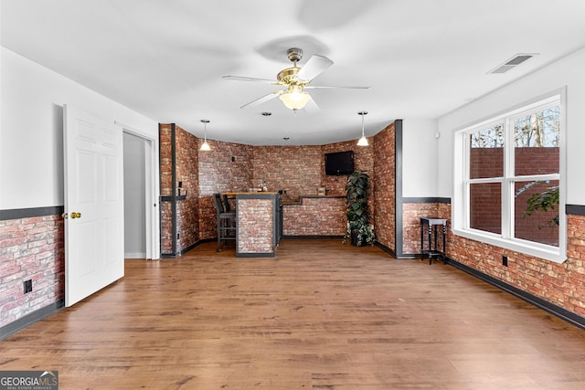 unfurnished living room with wainscoting, visible vents, brick wall, and wood finished floors