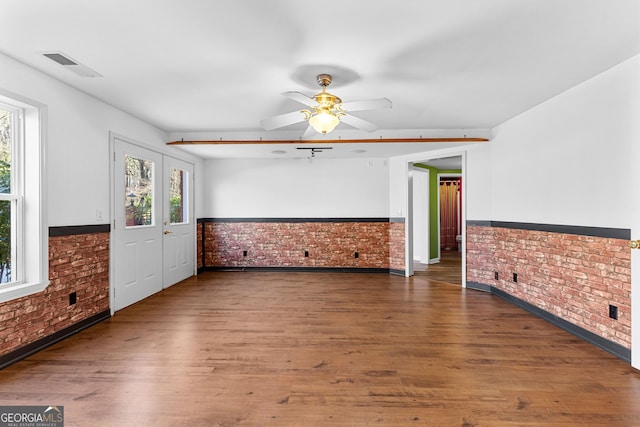 spare room featuring a wainscoted wall, visible vents, brick wall, and wood finished floors