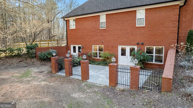 back of house featuring a fenced front yard, a gate, brick siding, and a shingled roof