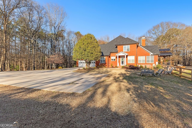 view of front of property featuring a chimney, fence, concrete driveway, and roof with shingles