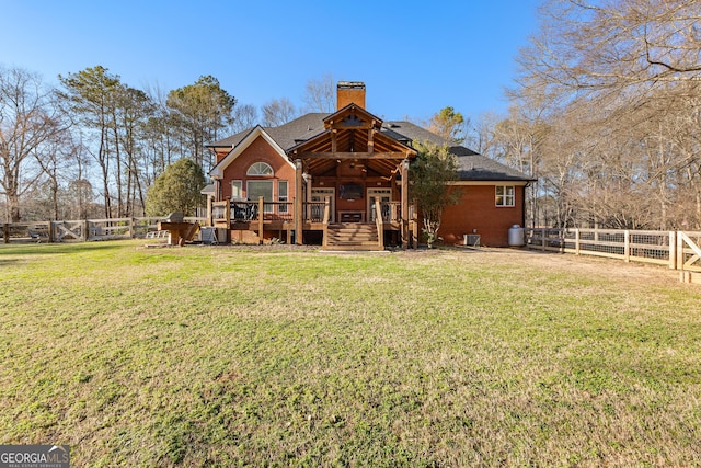 back of house featuring a lawn, a fenced backyard, a chimney, a deck, and brick siding