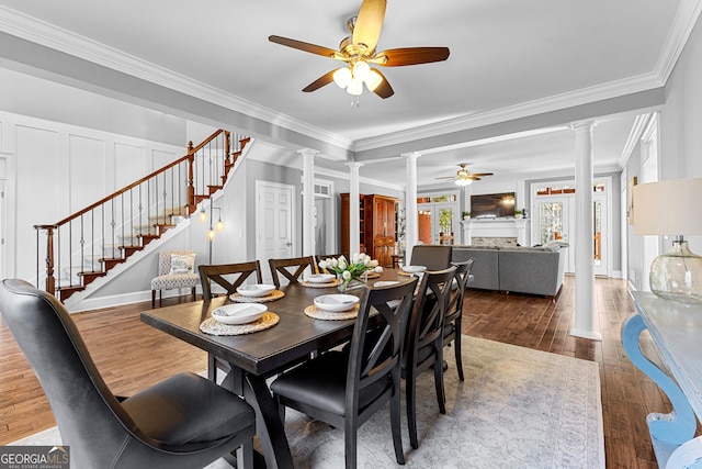 dining room featuring hardwood / wood-style flooring, a decorative wall, stairs, ornate columns, and crown molding