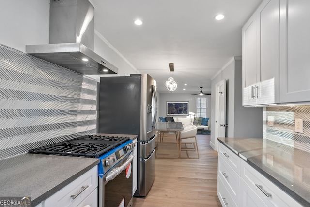 kitchen with stainless steel gas stove, backsplash, light wood-type flooring, wall chimney range hood, and white cabinets
