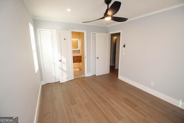 unfurnished bedroom featuring baseboards, a ceiling fan, wood finished floors, ensuite bathroom, and multiple closets