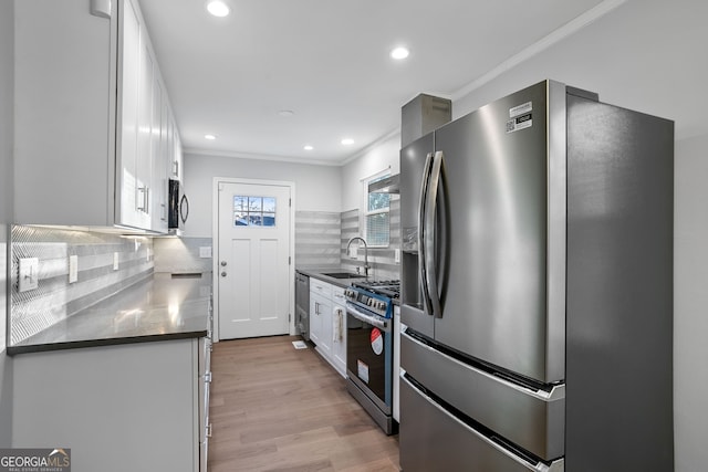 kitchen featuring stainless steel appliances, dark countertops, white cabinetry, a sink, and light wood-style floors