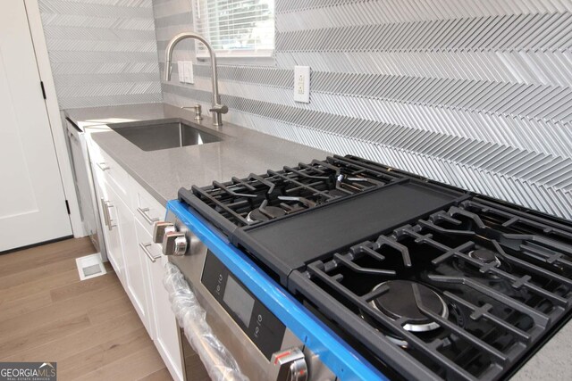kitchen featuring a sink, light wood finished floors, light stone countertops, stainless steel range with gas stovetop, and white cabinets