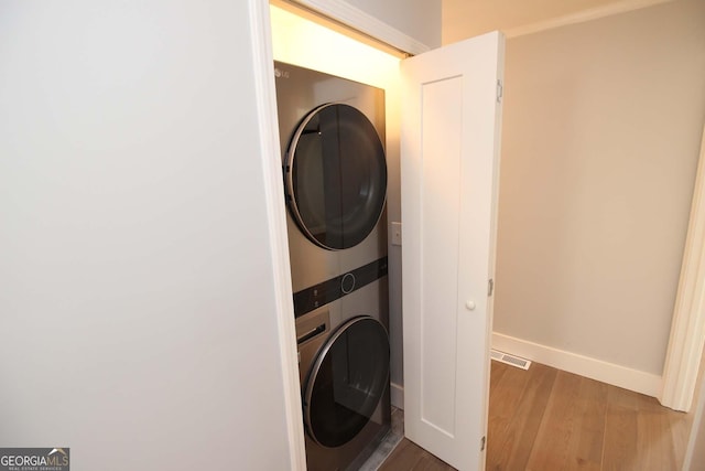 laundry room featuring baseboards, wood finished floors, stacked washer / drying machine, and laundry area