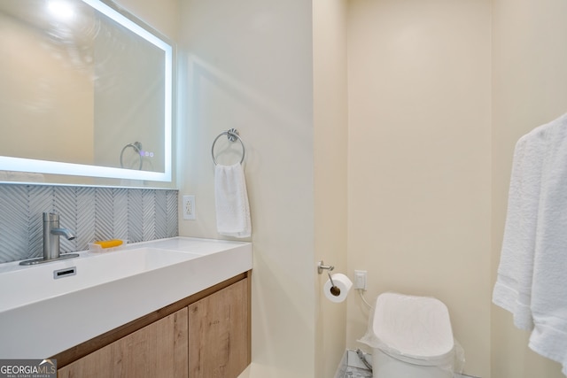half bath with toilet, vanity, and tasteful backsplash
