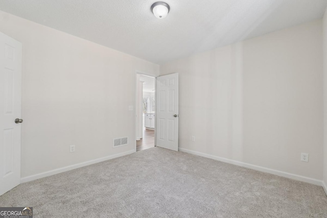 spare room featuring light carpet, a textured ceiling, visible vents, and baseboards