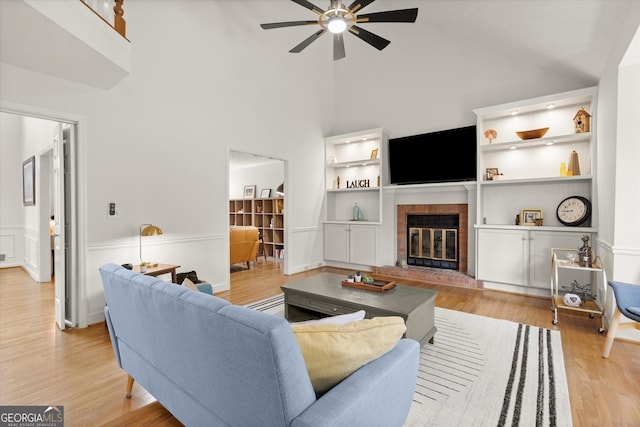 living area with light wood finished floors, ceiling fan, built in shelves, high vaulted ceiling, and a fireplace