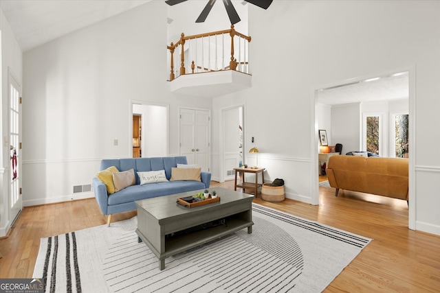 living area with visible vents, light wood-style floors, a ceiling fan, high vaulted ceiling, and baseboards