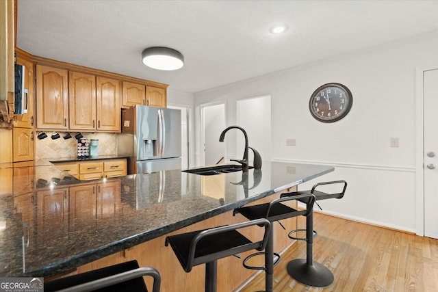 kitchen with a sink, light wood-style floors, stainless steel refrigerator with ice dispenser, backsplash, and a kitchen bar