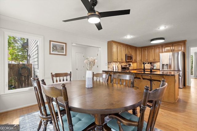 dining room featuring crown molding, baseboards, a ceiling fan, and light wood-style floors