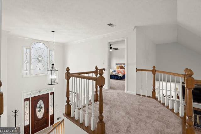 hallway featuring carpet floors, crown molding, a notable chandelier, visible vents, and an upstairs landing