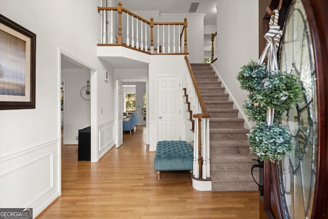 entrance foyer featuring ornamental molding, visible vents, a decorative wall, and light wood-style flooring