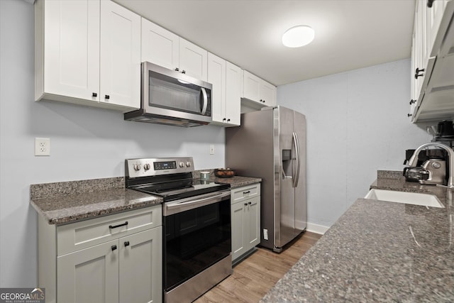 kitchen featuring appliances with stainless steel finishes, white cabinetry, a sink, dark stone counters, and light wood-type flooring