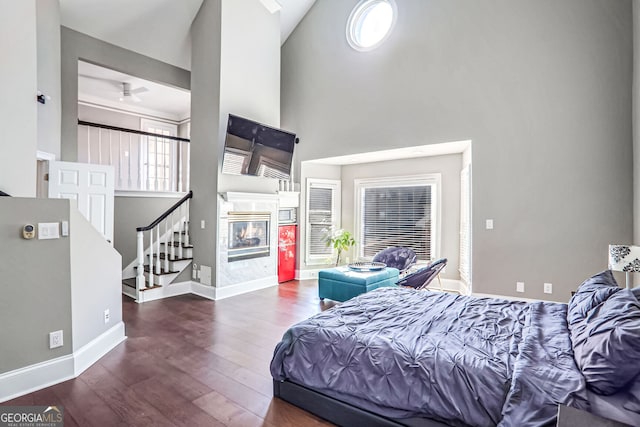 bedroom featuring baseboards, a glass covered fireplace, dark wood-type flooring, access to outside, and high vaulted ceiling