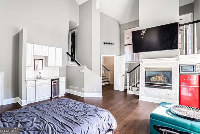 bedroom featuring wine cooler, dark wood-style flooring, a fireplace, a sink, and high vaulted ceiling