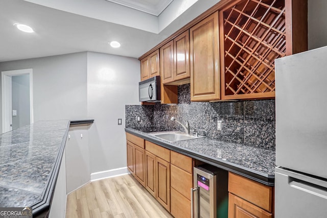 kitchen featuring backsplash, brown cabinetry, freestanding refrigerator, a sink, and black microwave