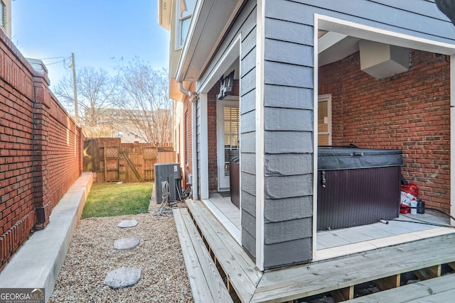 exterior space featuring central AC, brick siding, a fenced backyard, and a hot tub