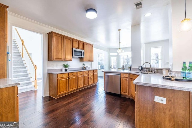 kitchen with stainless steel appliances, a peninsula, a sink, hanging light fixtures, and brown cabinetry