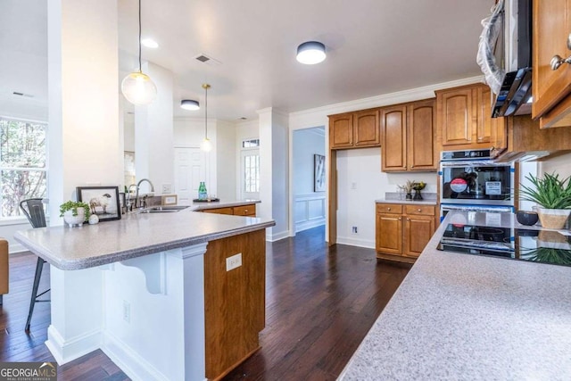 kitchen featuring brown cabinetry, a breakfast bar, decorative light fixtures, a sink, and black gas stovetop