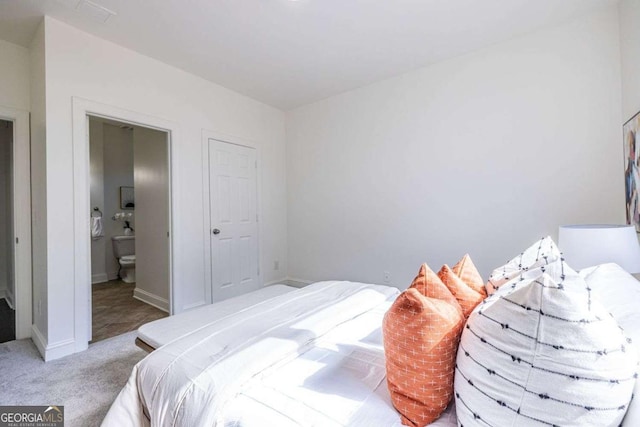 carpeted bedroom with ensuite bathroom and baseboards