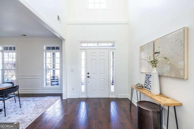 foyer with crown molding, dark wood finished floors, visible vents, a towering ceiling, and baseboards