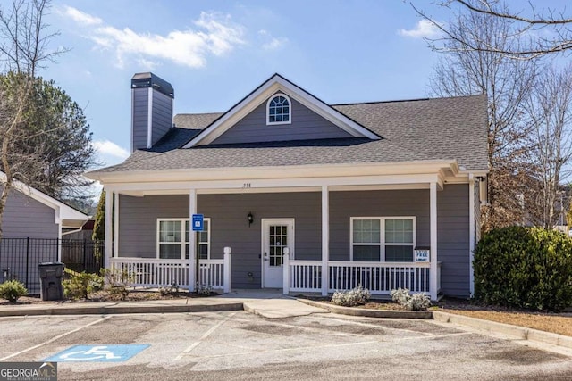 bungalow-style home with covered porch, a shingled roof, a chimney, and uncovered parking