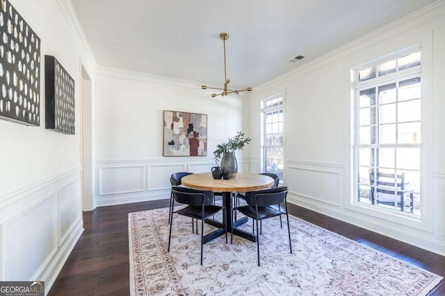 dining space featuring dark wood-style floors, a decorative wall, visible vents, and crown molding