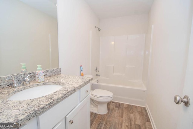 bathroom featuring toilet, vanity, wood finished floors,  shower combination, and baseboards