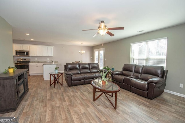 living room featuring light wood-style floors, visible vents, baseboards, and ceiling fan with notable chandelier