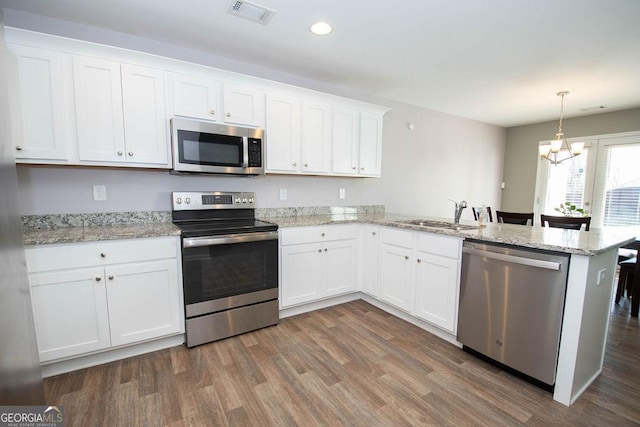 kitchen with a peninsula, visible vents, white cabinetry, appliances with stainless steel finishes, and decorative light fixtures