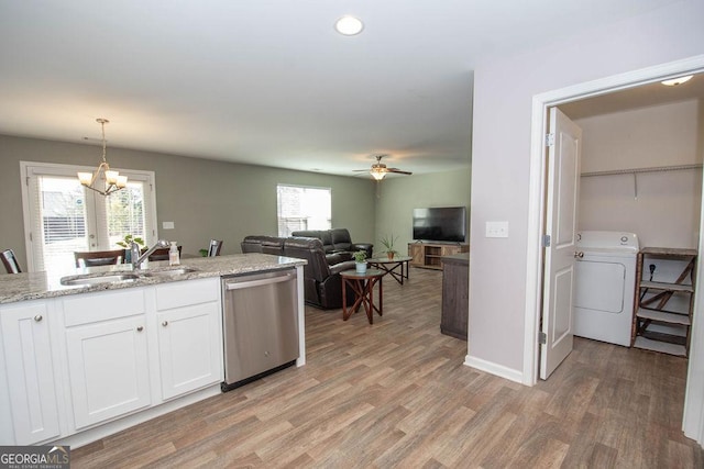 kitchen with hanging light fixtures, stainless steel dishwasher, white cabinets, a sink, and washer / dryer