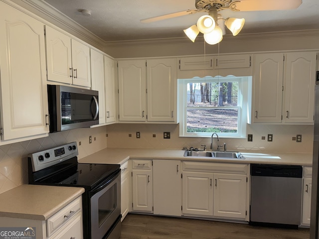 kitchen with a sink, white cabinetry, light countertops, appliances with stainless steel finishes, and crown molding