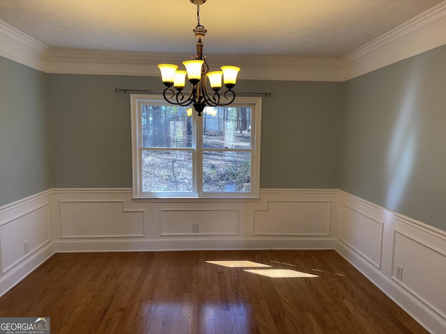 unfurnished dining area with a wainscoted wall, ornamental molding, dark wood-style flooring, and an inviting chandelier