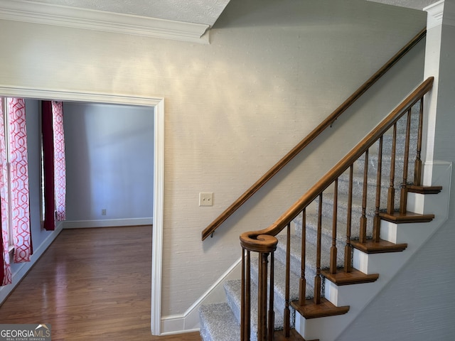 staircase featuring baseboards, a textured ceiling, ornamental molding, and wood finished floors