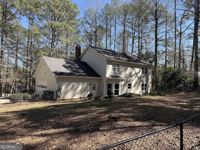 view of side of home featuring a garage, fence, and a chimney