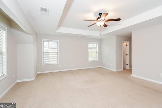 unfurnished room with a raised ceiling, light colored carpet, visible vents, ceiling fan, and baseboards