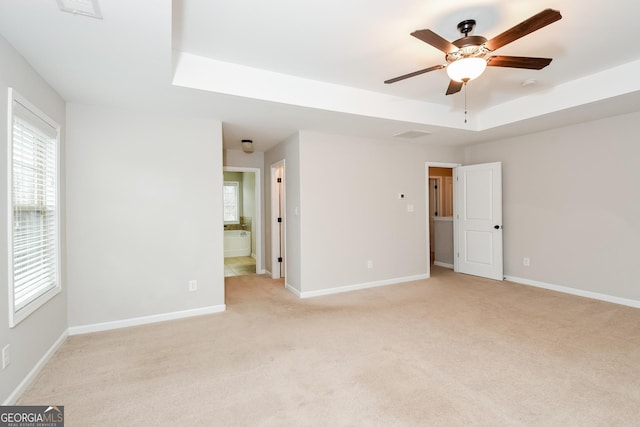 interior space featuring a raised ceiling, light carpet, visible vents, and baseboards