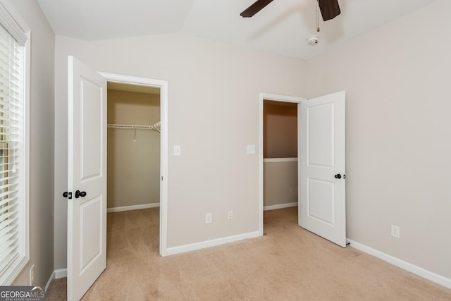 unfurnished bedroom with light carpet, baseboards, a walk in closet, and lofted ceiling